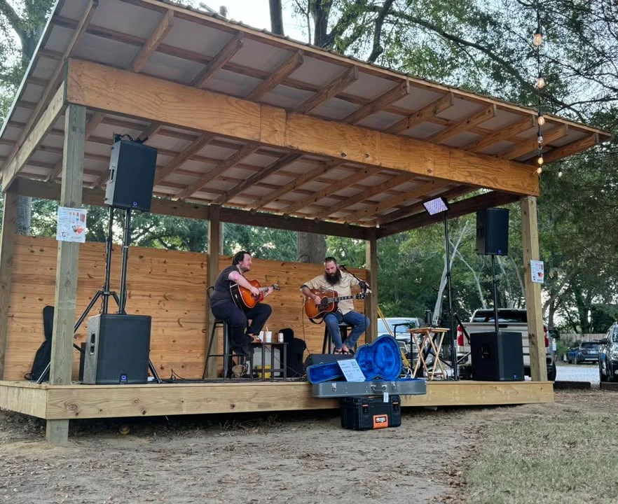 An outdoor stage lit with subtle blue light.  It is set up for a band with a drumkit and microphones