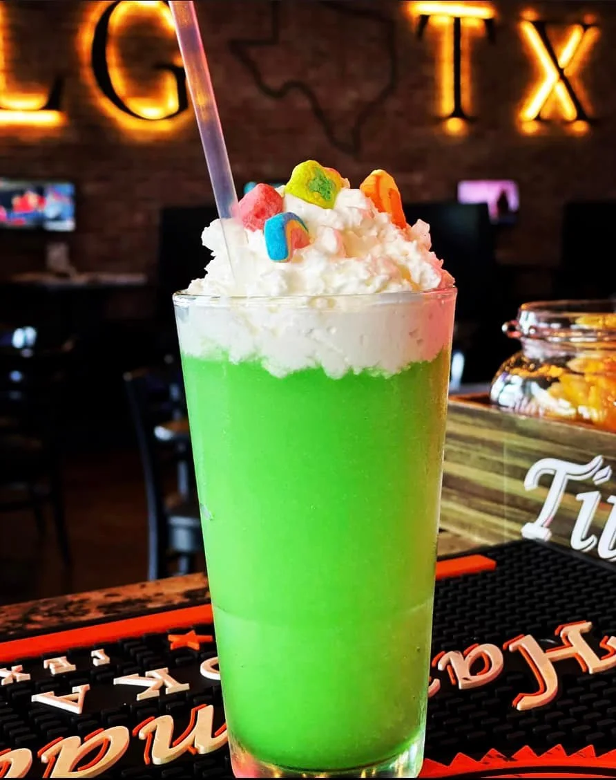 A bright green drink topped with whipped cream and colorful candy pieces, served in a clear glass.