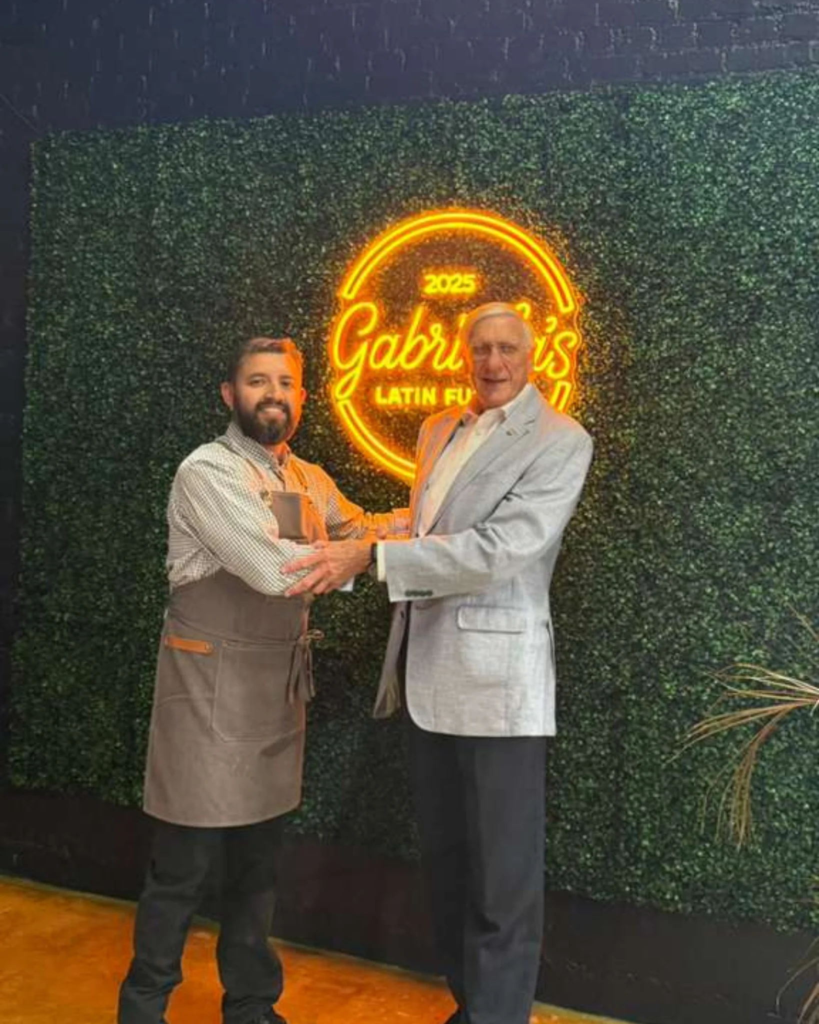 Two chefs shaking hands in front of a vibrant restaurant sign