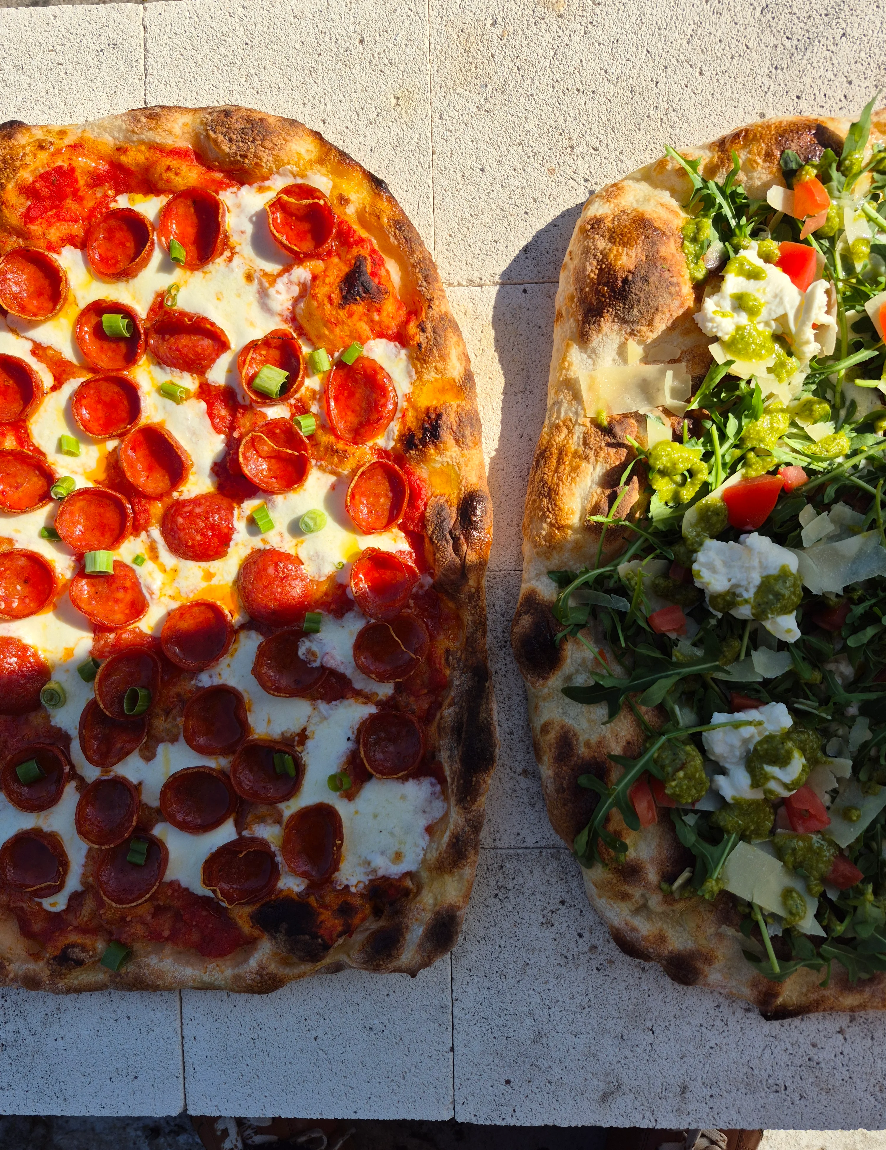 Pepperoni pizza and arugula salad pizza on a rustic stone surface