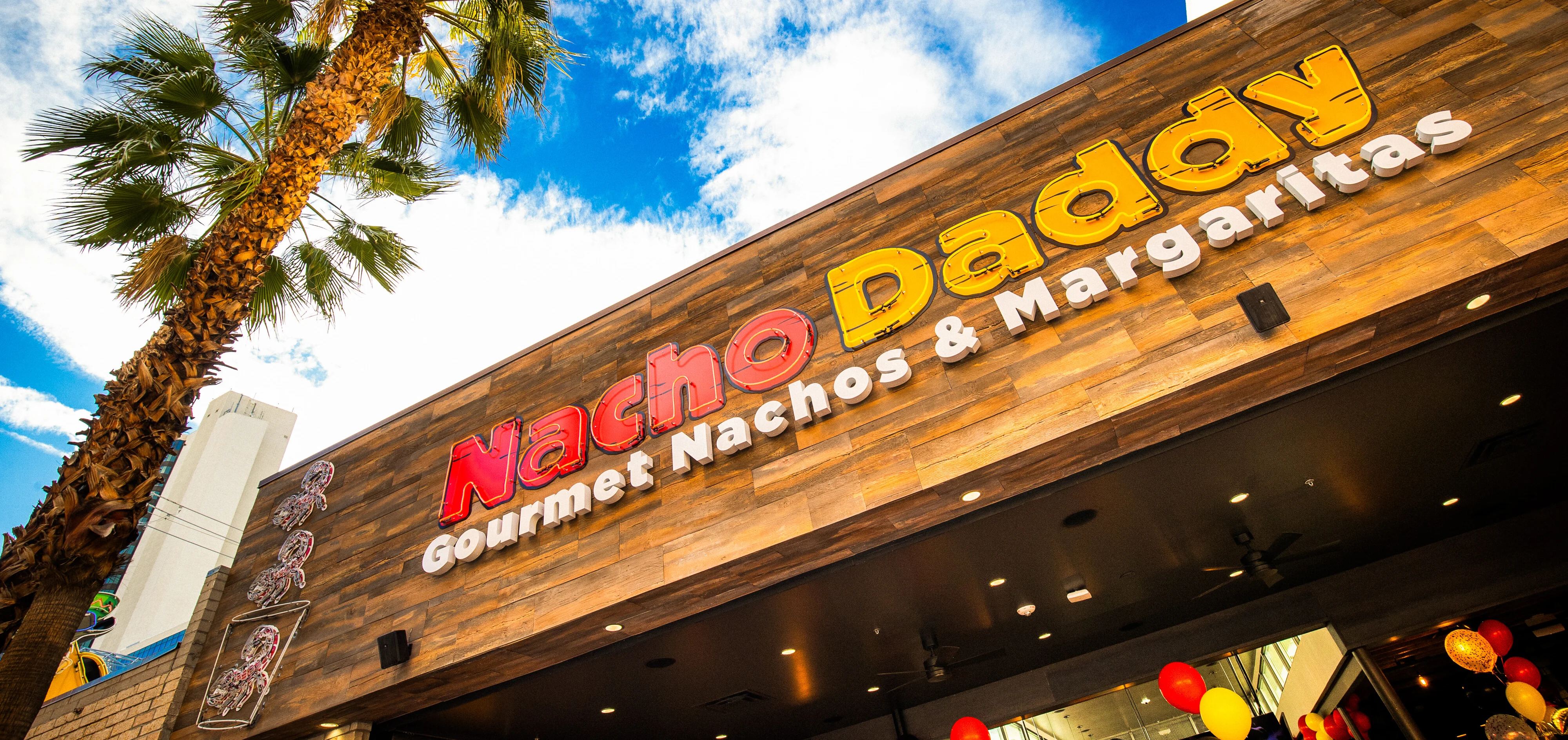 Exterior view of Nacho Daddy restaurant with palm trees and blue sky