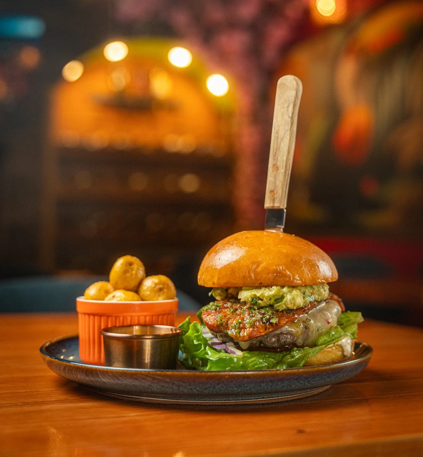 Gourmet burger with toppings and side potatoes on a rustic plate
