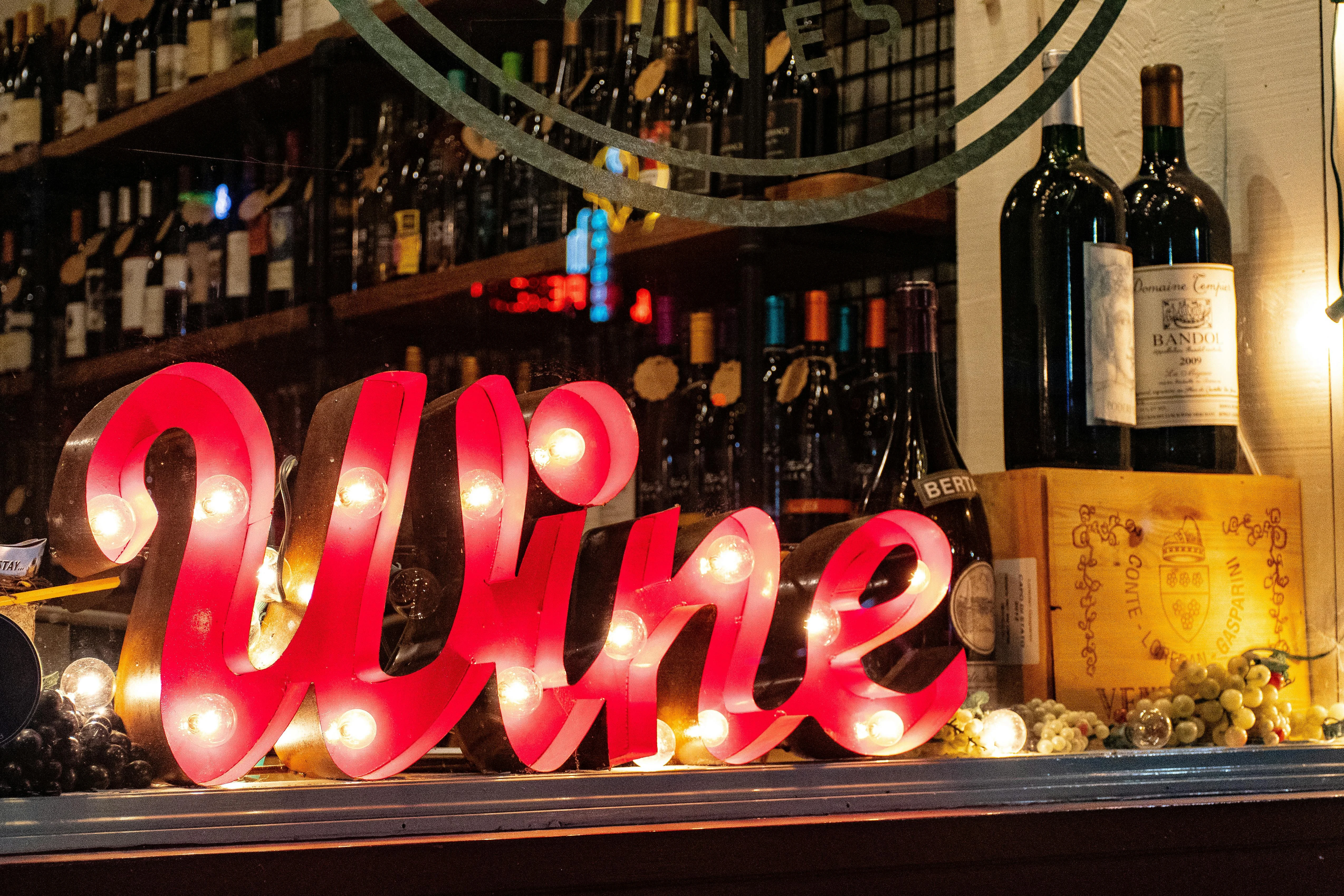 Illuminated 'Wine' sign in a cozy wine shop with bottles in the background.