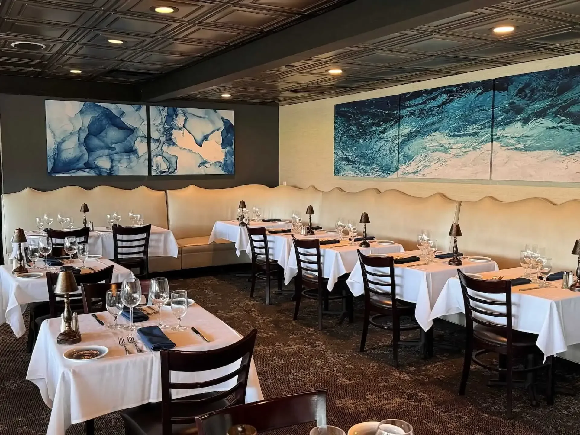 An elegant restaurant dining area with neatly set tables, featuring artistic wall decor and ambient lighting.
