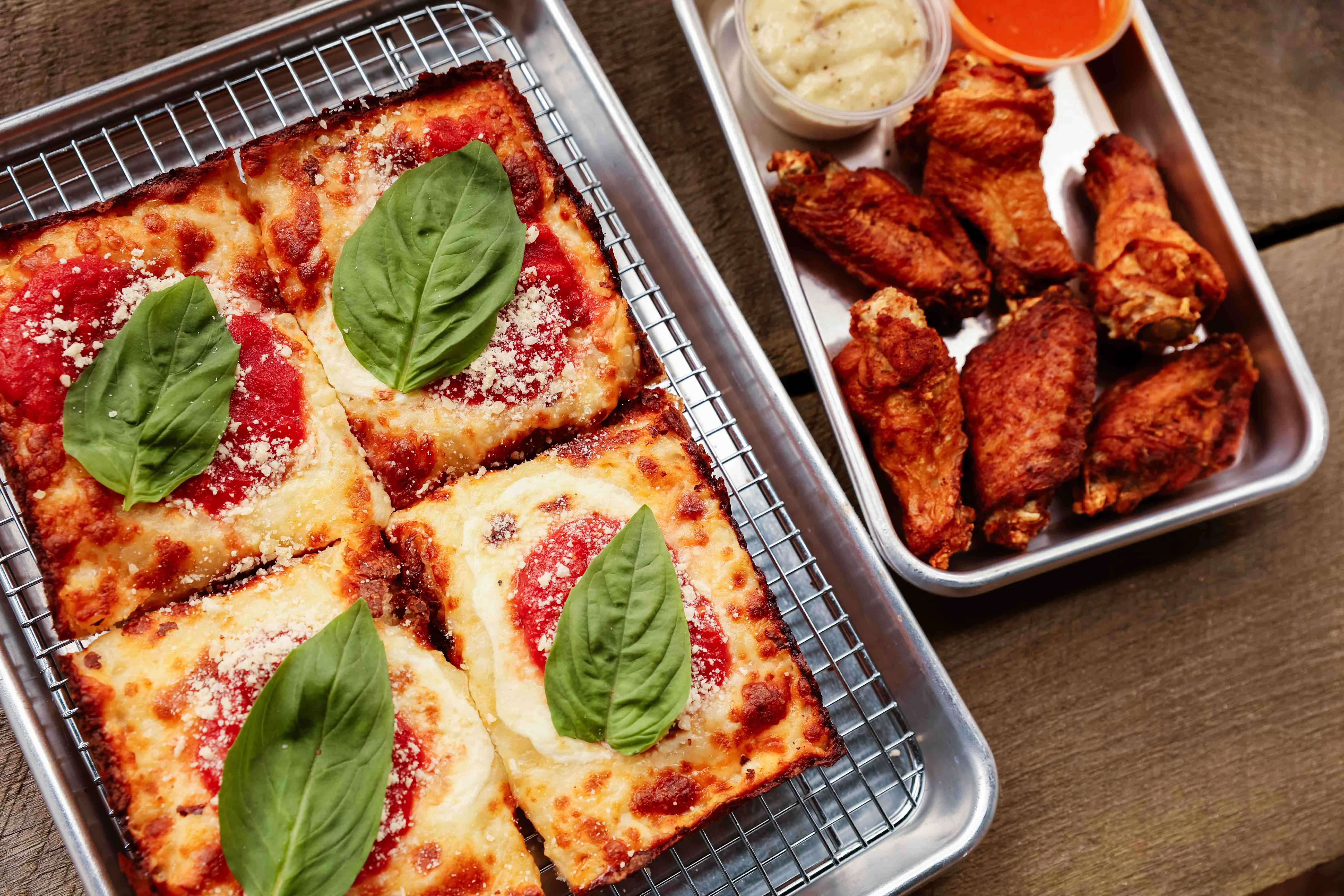 Detroit-style pizza with fresh basil and chicken wings