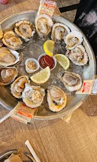 A platter of fresh oysters presented on ice, garnished with lemon wedges and accompanied by dipping sauces.