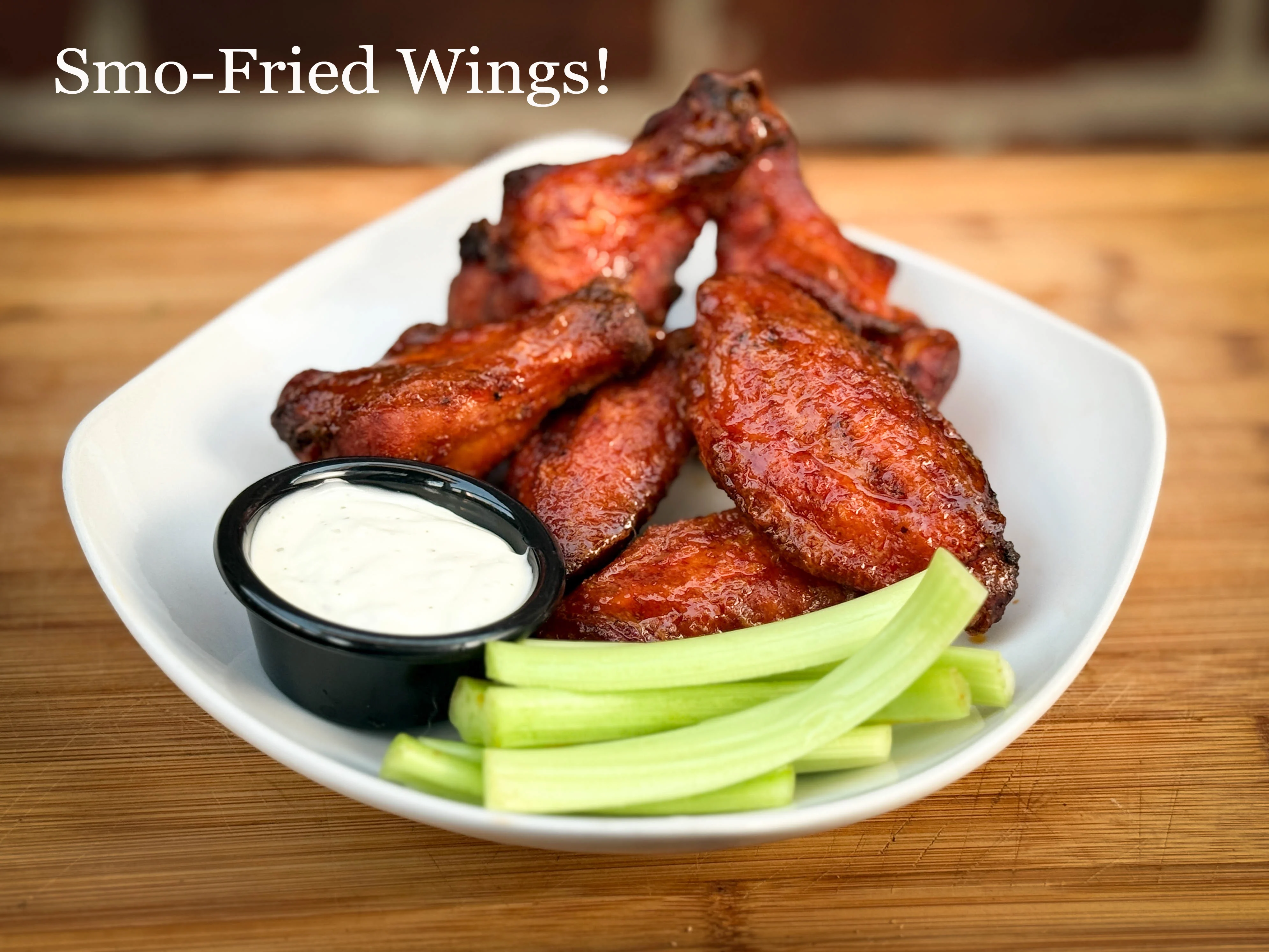 A plate of crispy chicken wings accompanied by celery sticks and a small bowl of dipping sauce.
