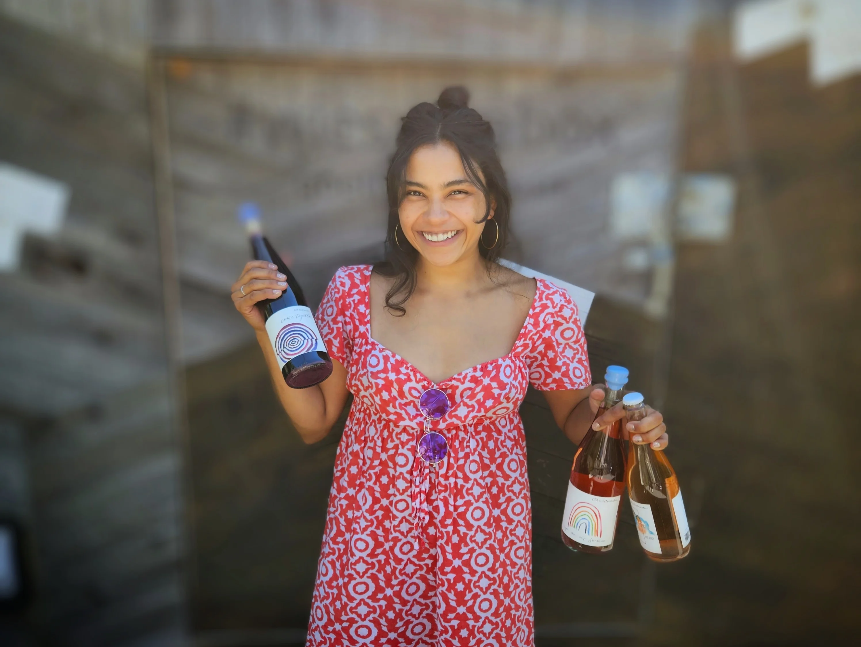 Smiling woman holding bottles of wine in a vibrant dress