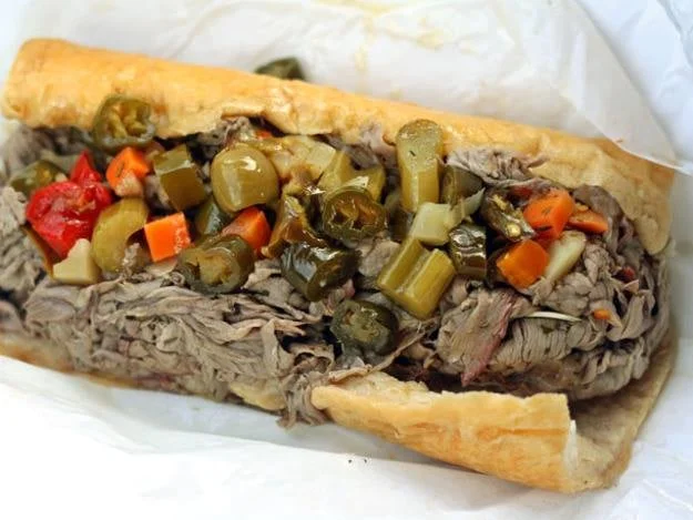 A sandwich filled with shredded beef and topped with various pickled vegetables, served in a crusty roll.