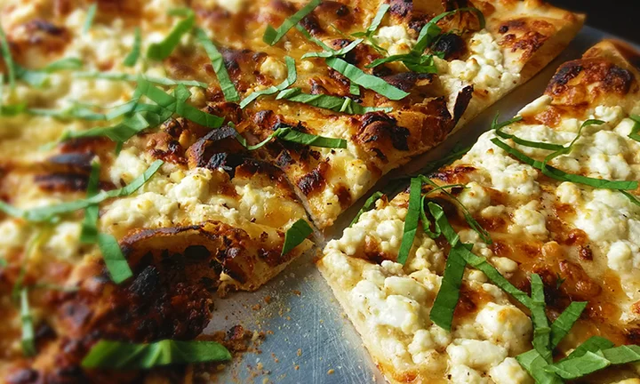 A close-up of a pizza with a golden crust, topped with melted cheese and fresh basil, ready to be sliced.