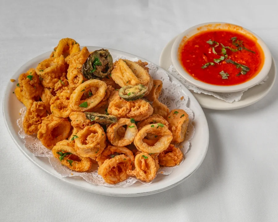 Plate of golden fried calamari garnished with herbs, accompanied by a bowl of vibrant red marinara sauce with green garnish, evoking a delicious, savory experience served at Toscana on Main