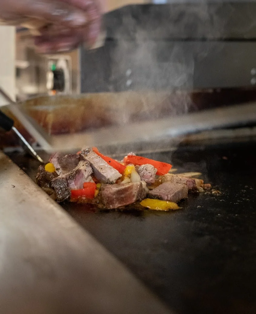 A delicious flat top grill with various grilled meats and vegetables.