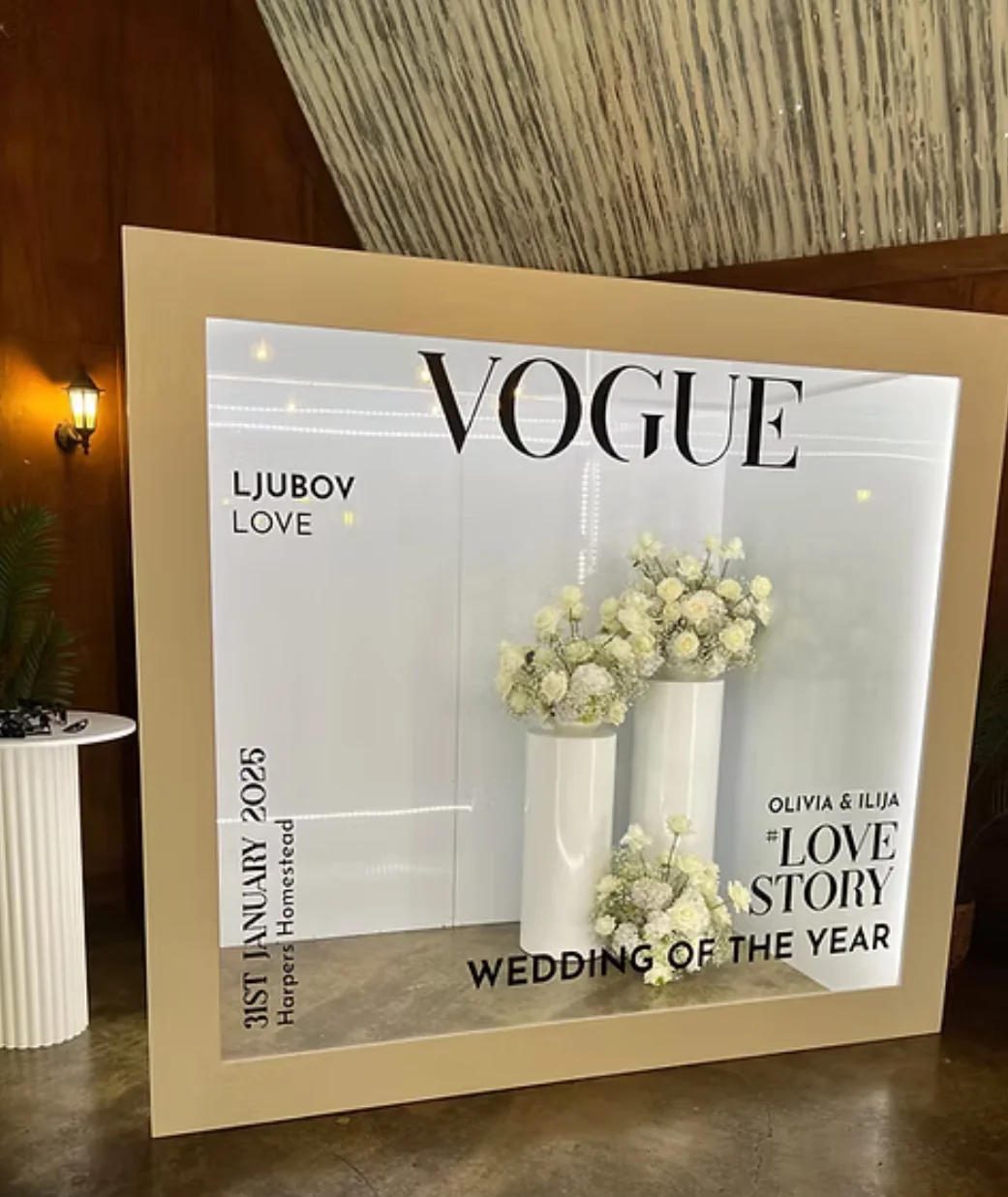 A stylish wedding display with floral arrangements in white vases, featuring a backdrop that promotes the event as a 'Wedding of the Year'.