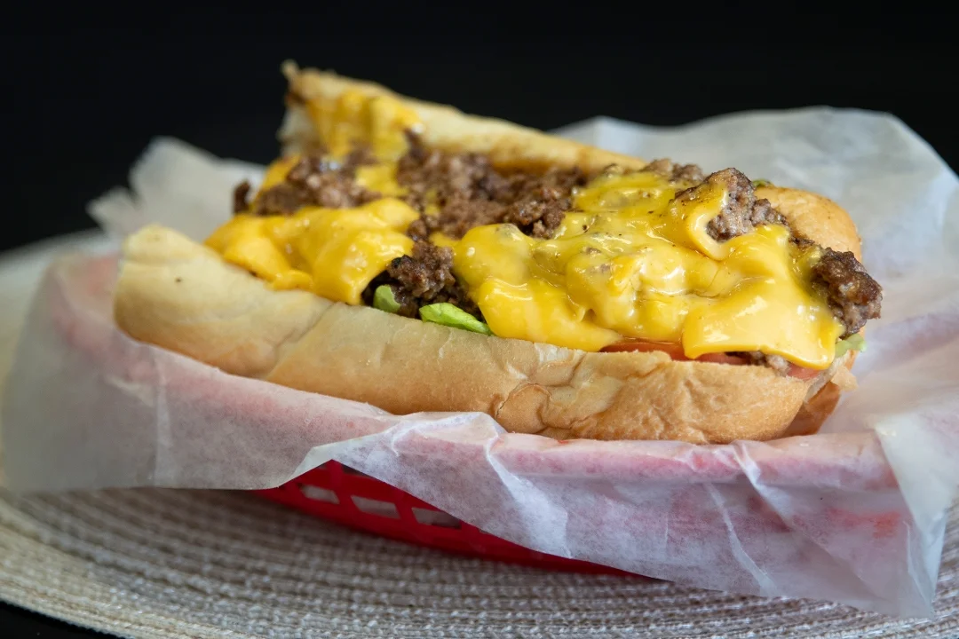 A sandwich filled with ground beef and melted cheese, garnished with lettuce, served in a red basket.