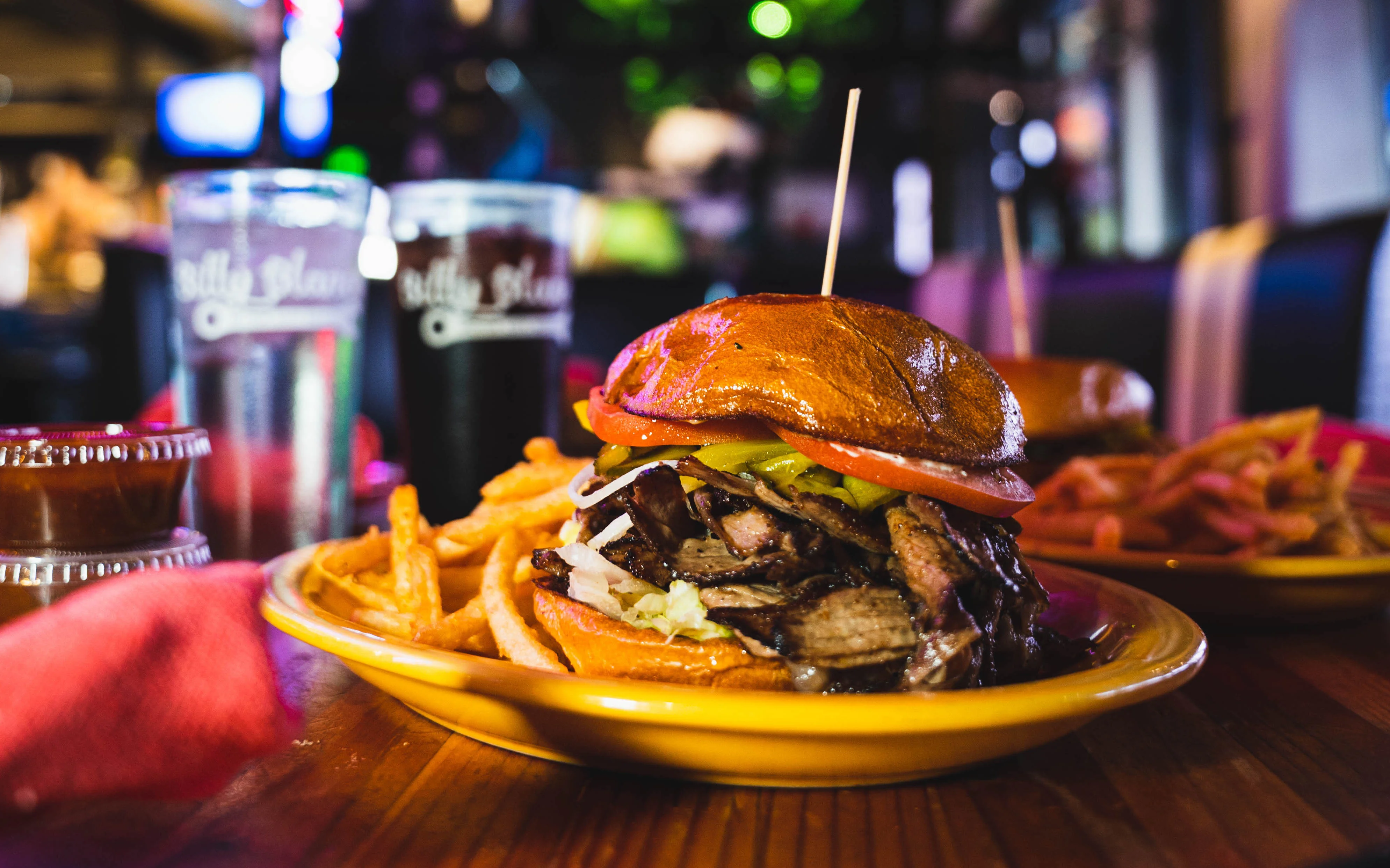 The Benji Burger is made with  double smash patties, shaved short rib, chipotle mayo, lettuce, tomato, crispy onion rings, house kansas city bbq sauce on grilled bun, select cheddar, american or blue cheese