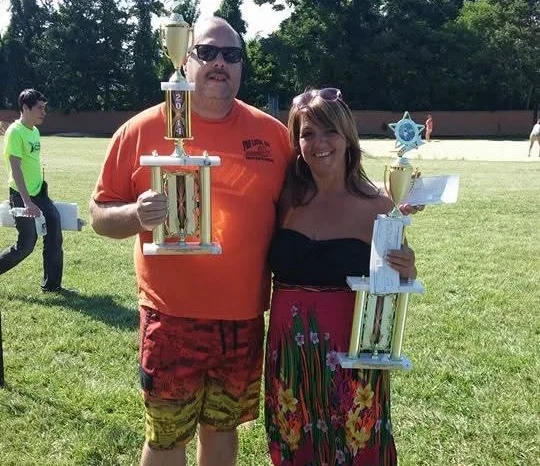 Two winners holding trophies at an outdoor event