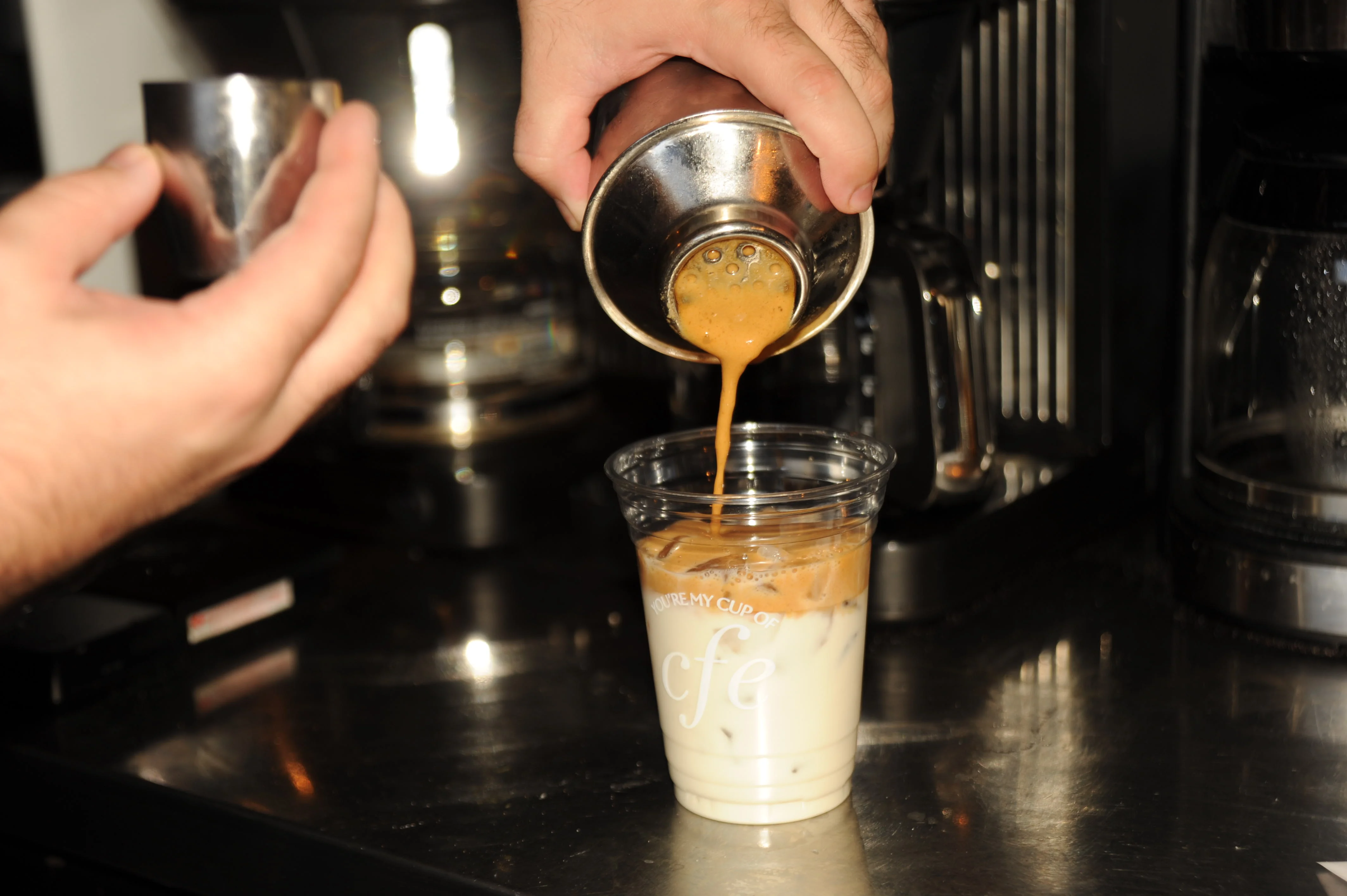 Barista pouring espresso over iced milk for a coffee drink