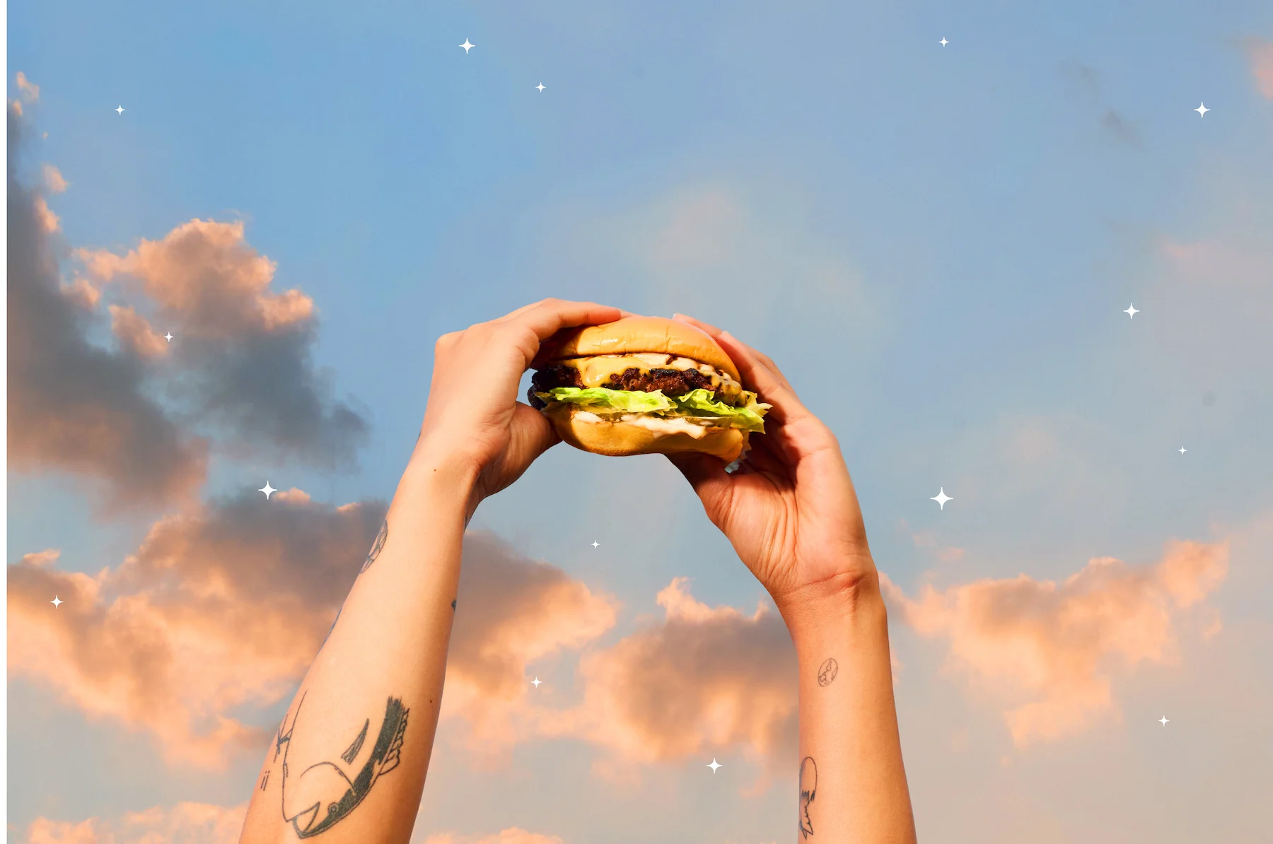 Hand holding a classic cheeseburger against a colorful sky