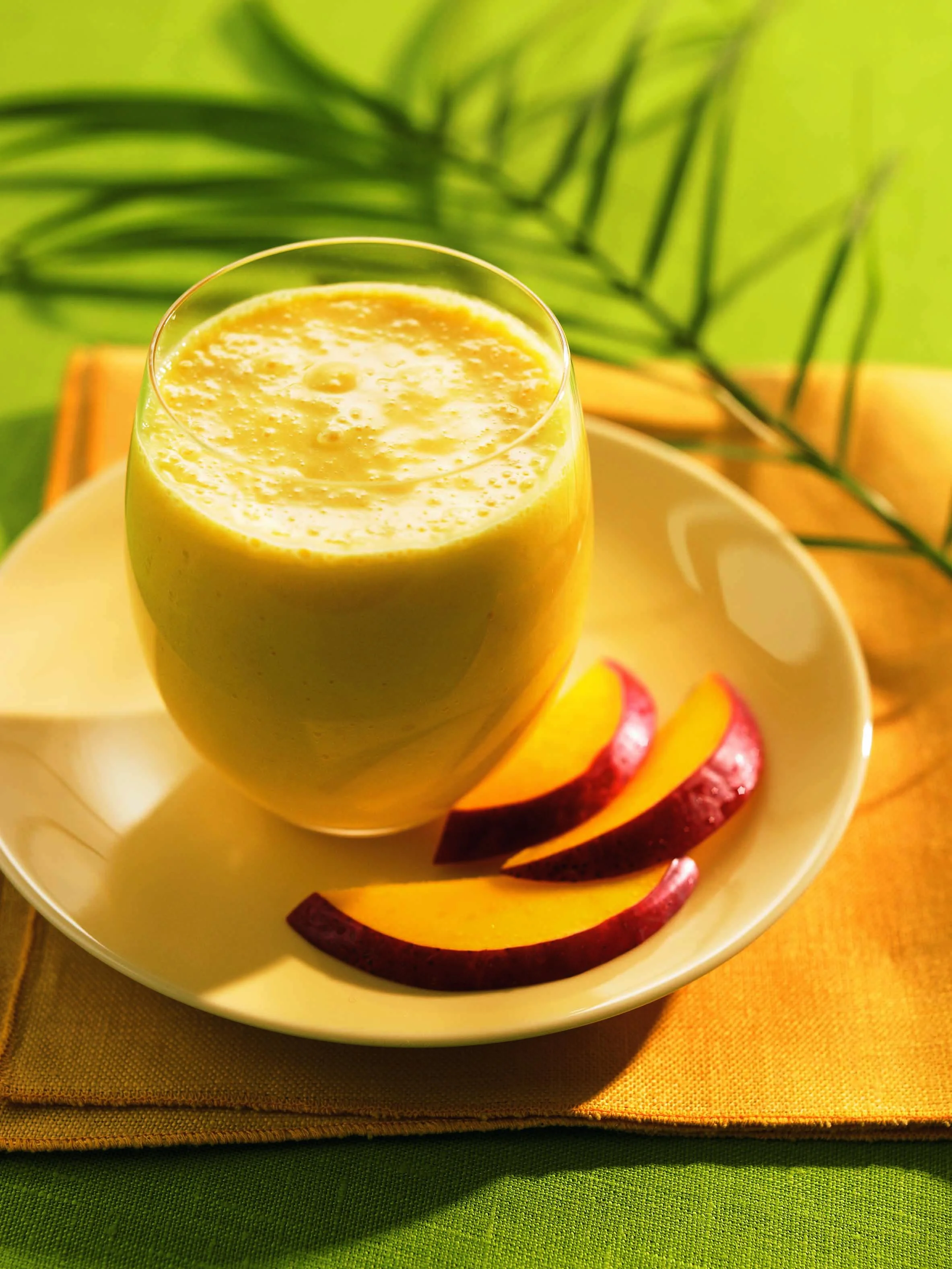 A refreshing smoothie served in a glass, accompanied by slices of fresh fruit on a plate. The colorful presentation includes vibrant colors of green and yellow.