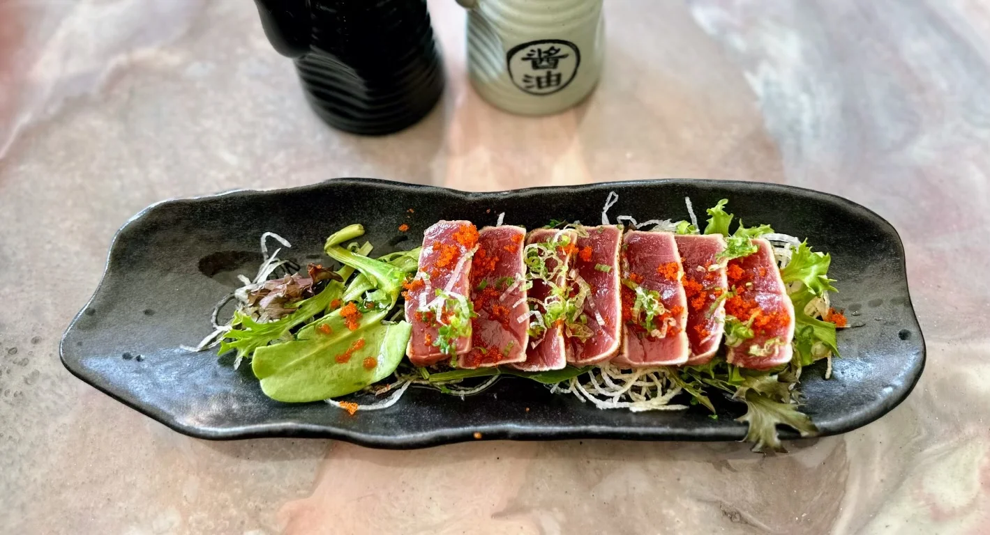 Japanese tuna tataki served over greens on a black ceramic plate