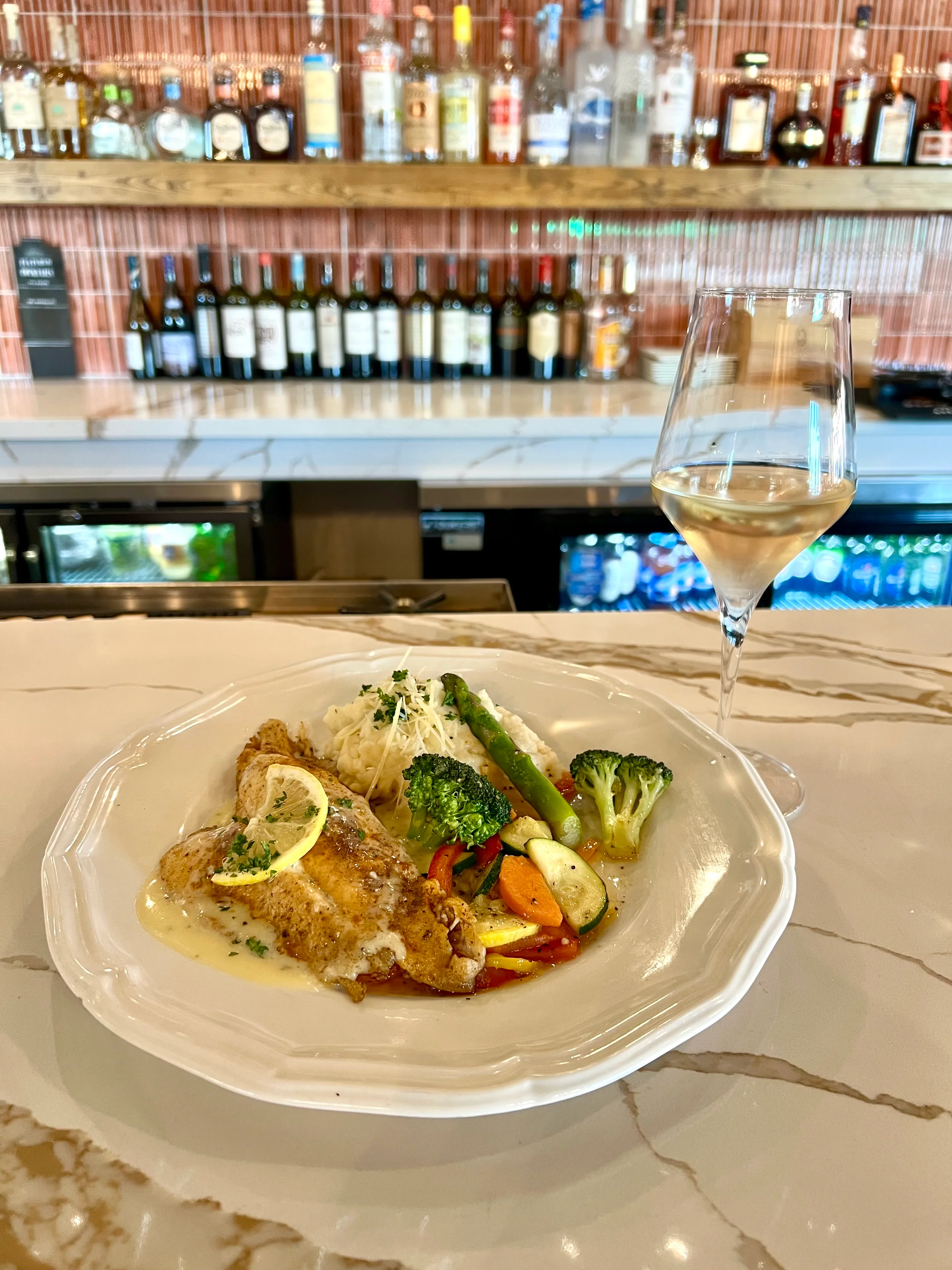 A plate of fried fish with lemon, served with seasonal vegetables and mashed potatoes, paired with a glass of white wine.