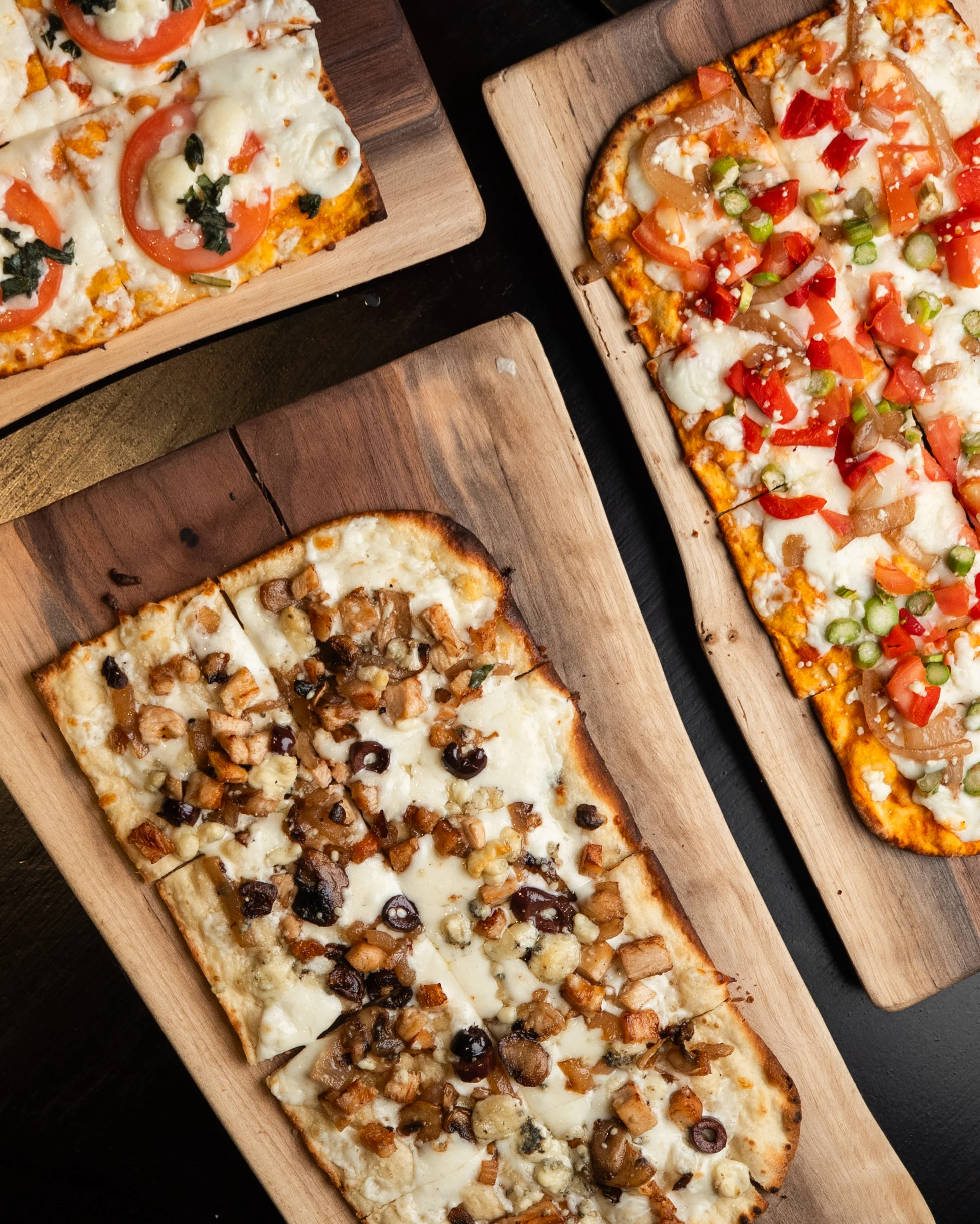 Three flatbreads with various toppings on wooden boards.