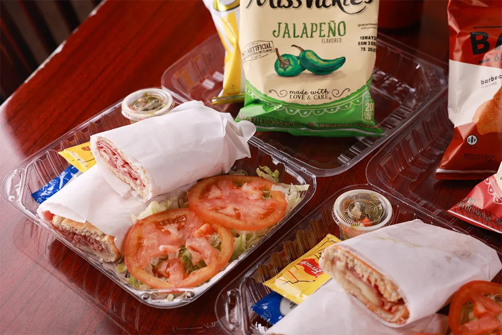 Two wrapped sandwiches with lettuce and tomato, chips, and condiments.