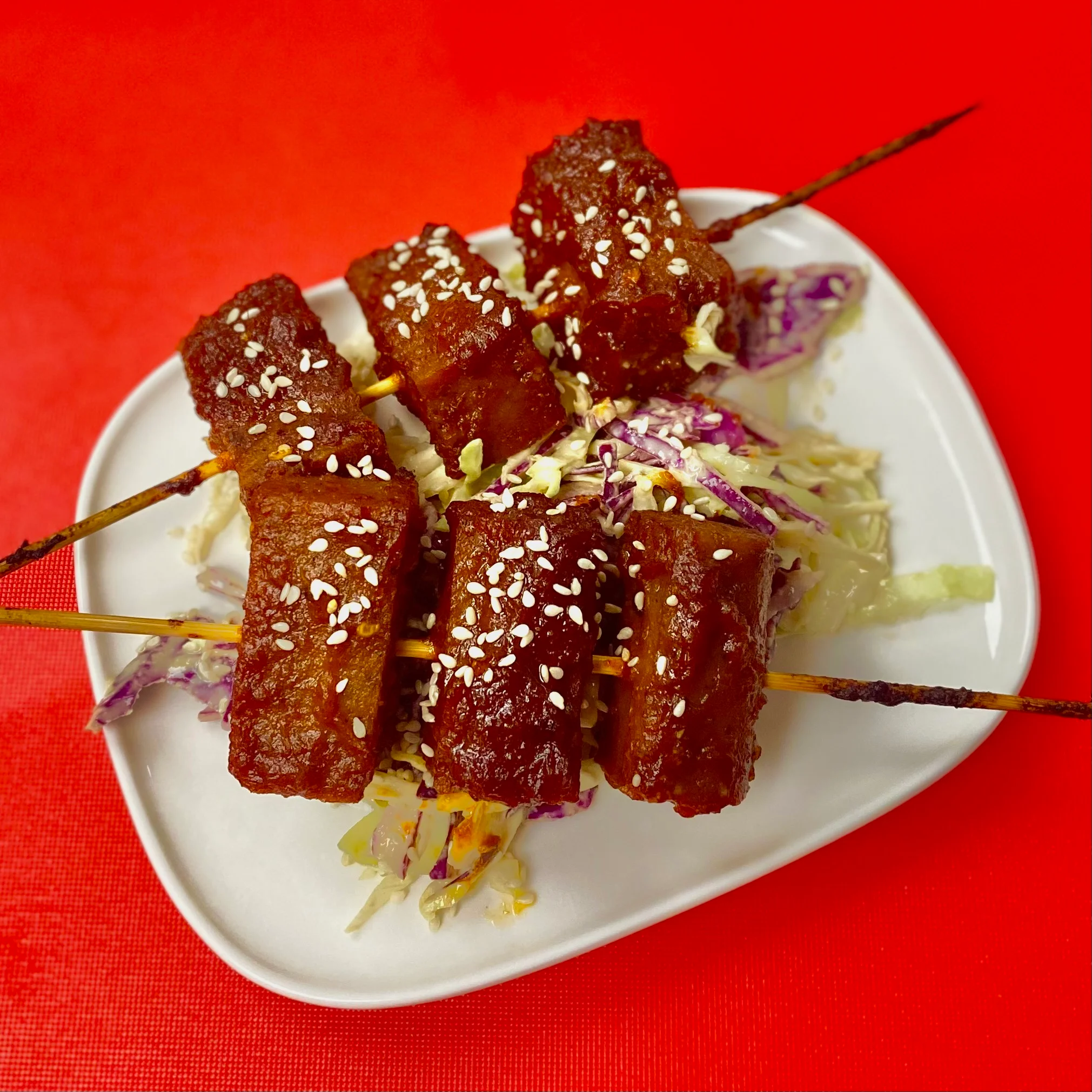 A plate of skewered meat pieces garnished with sesame seeds, served on a bed of shredded cabbage.