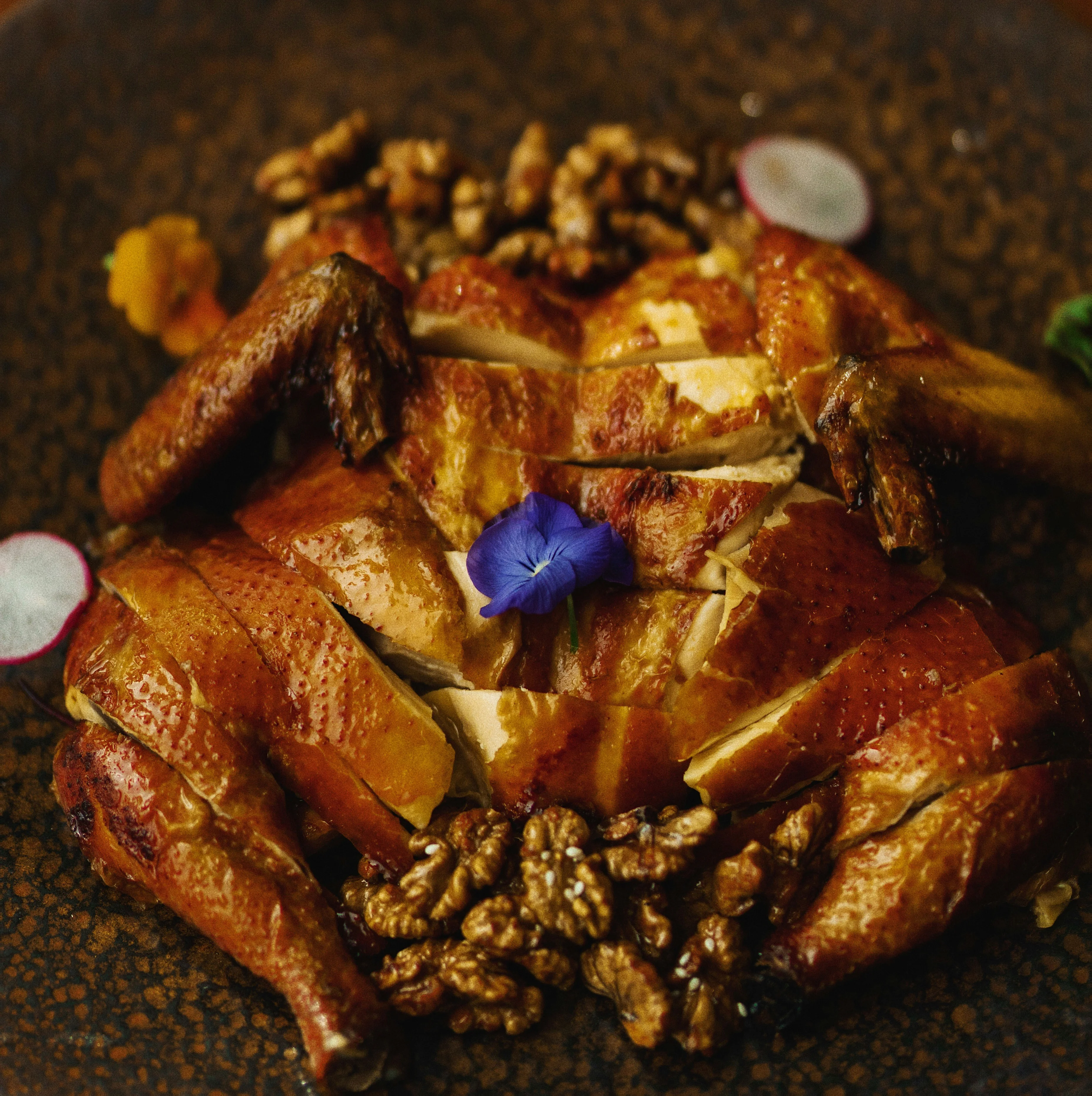 Crispy Chinese-style roasted chicken garnished with walnuts and edible flowers