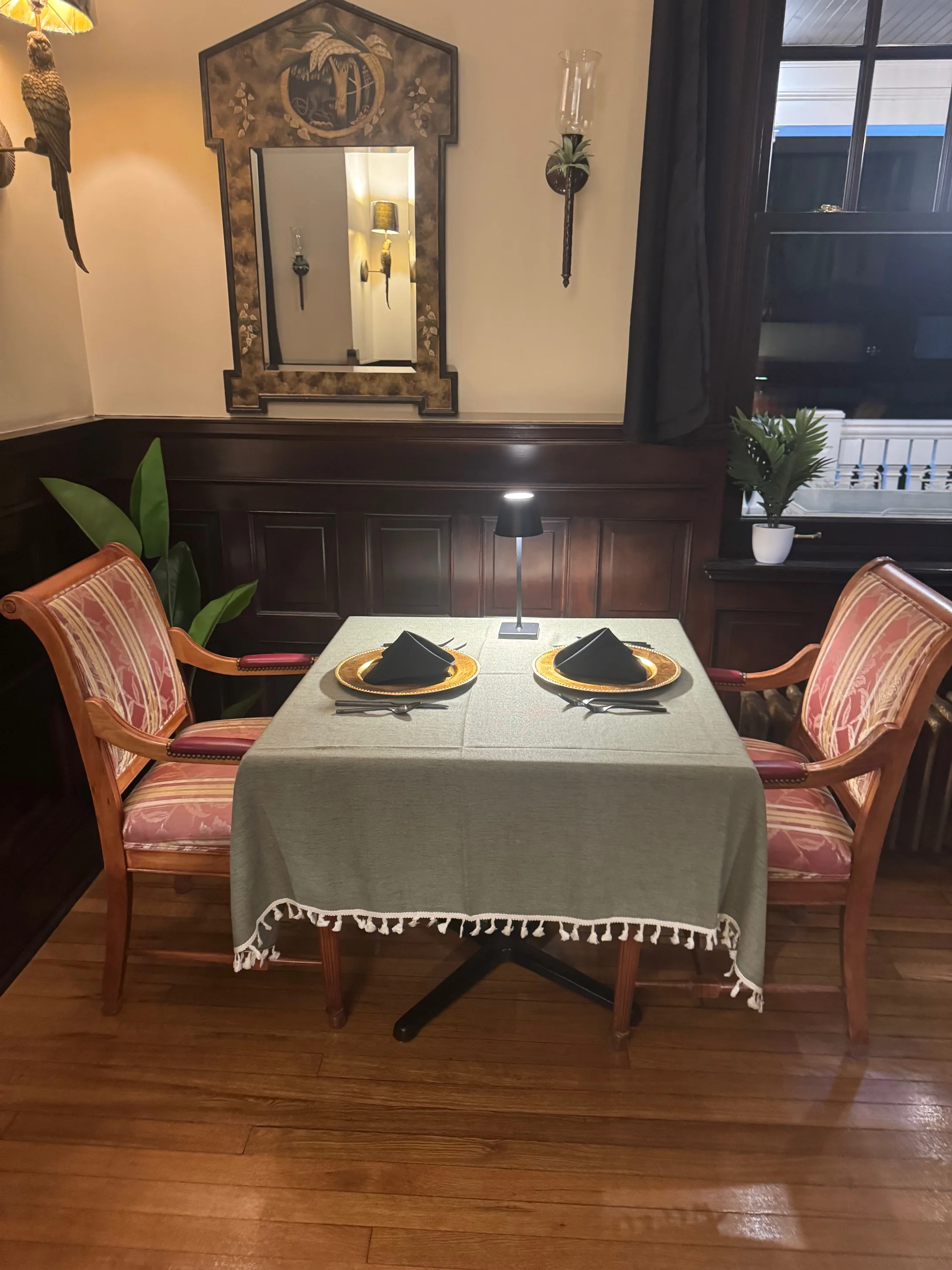 A small, intimate dining table set for two, complete with neatly arranged plates and a decorative mirror above.