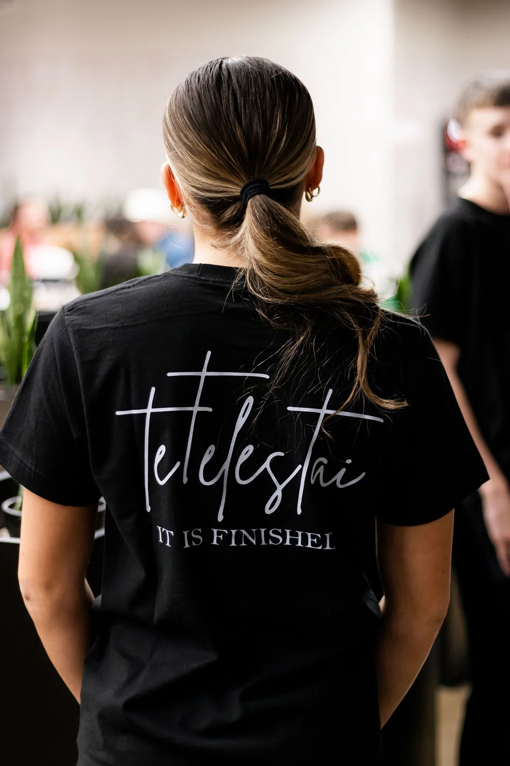 Back view of a person wearing a black shirt with 'Tetelestai' text