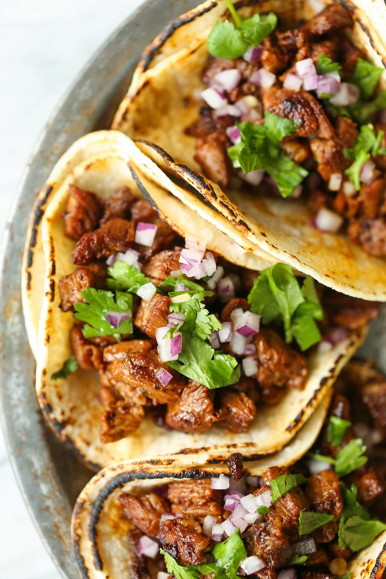 A close-up of delicious tacos filled with seasoned meat, garnished with onions and cilantro, served on a rustic plate.