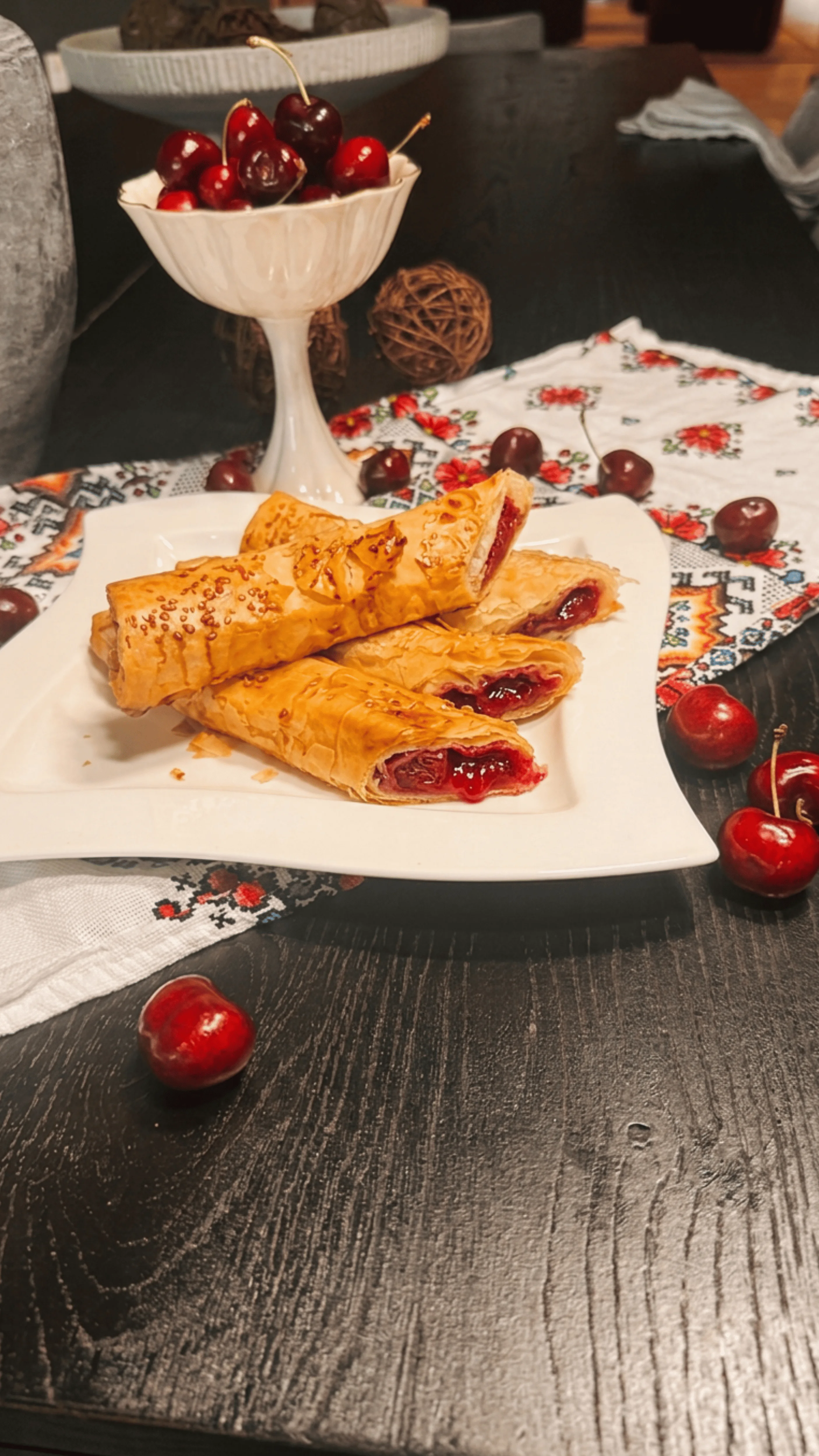 A plate of rolled pastry filled with cherry jam, served alongside fresh cherries.