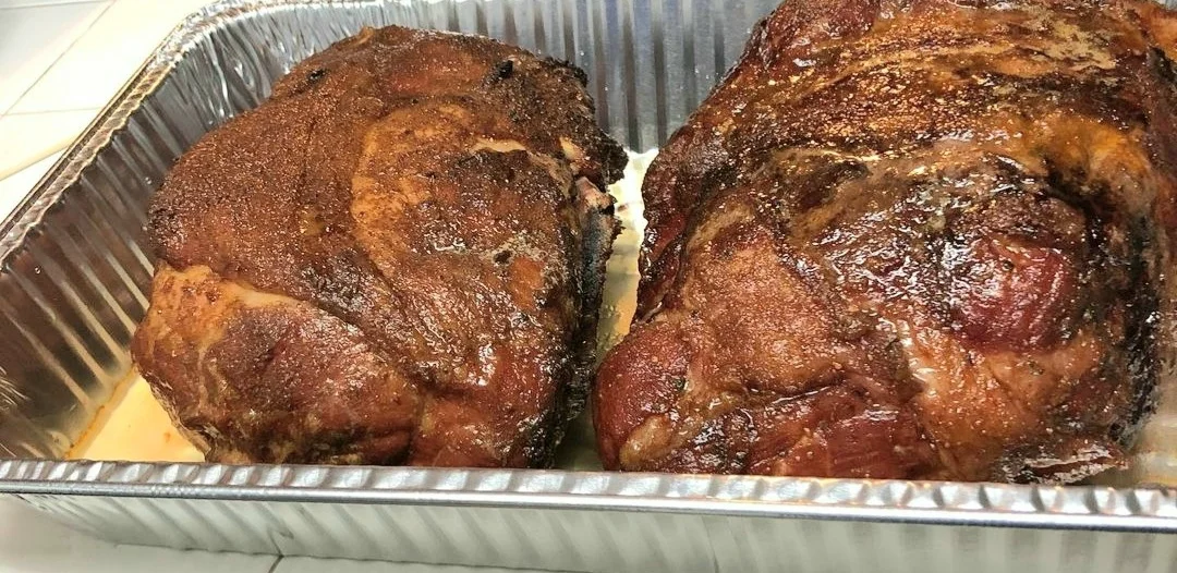 Two pieces of smoked meat resting in a tray, featuring a dark, caramelized crust.