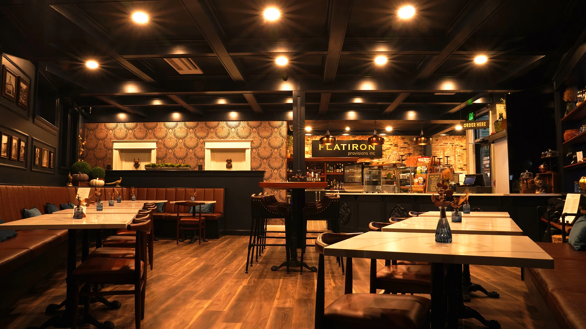 Dining room and order counter inside Flatiron Provisions Inc. restaurant, showcasing cozy booth seating, coffered dark wood ceilings, and exposed brick decor.