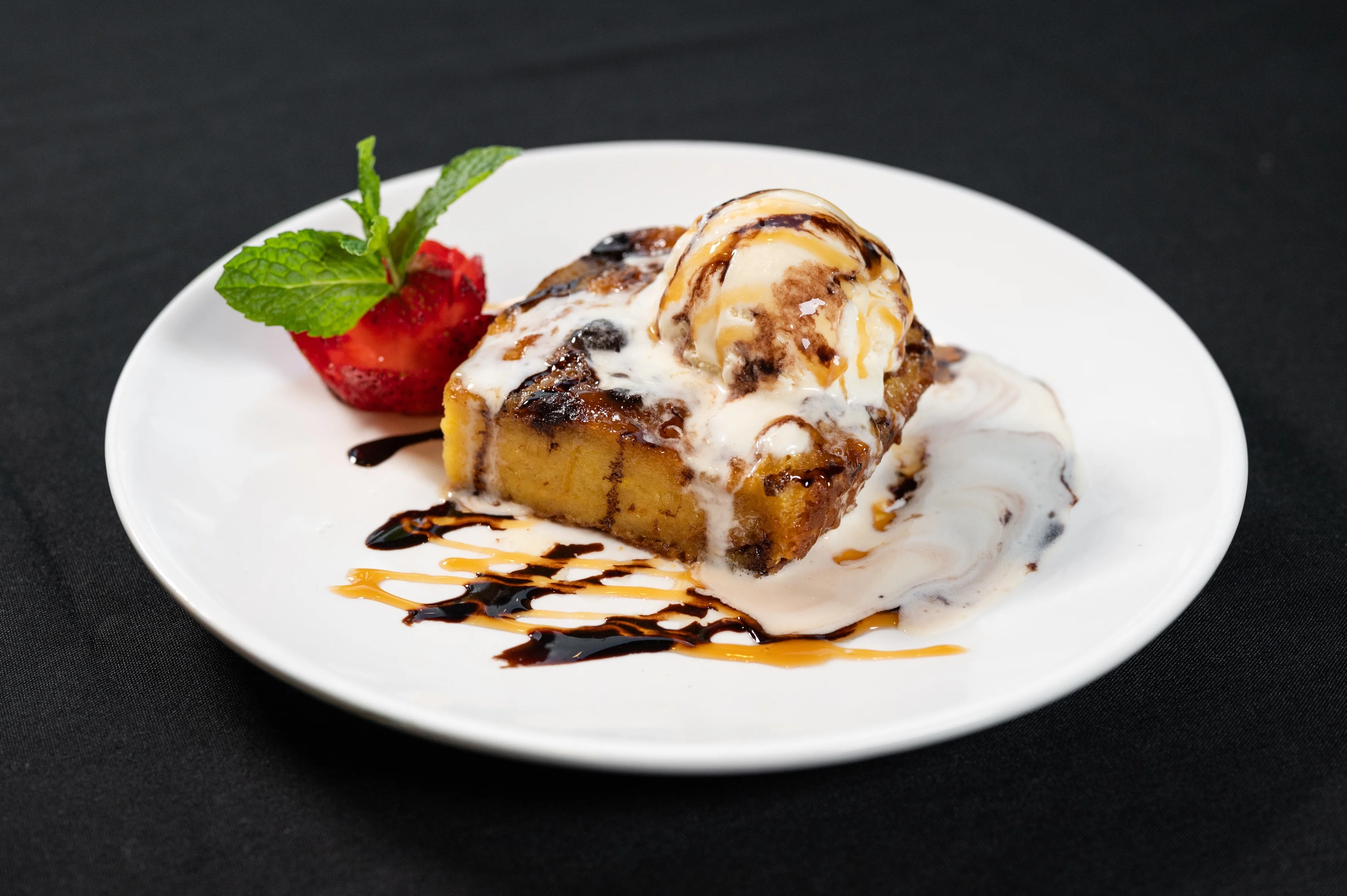 Delicious dessert featuring warm bread pudding topped with vanilla ice cream, chocolate sauce, and a fresh strawberry garnish served at Toscana on Main Westchester