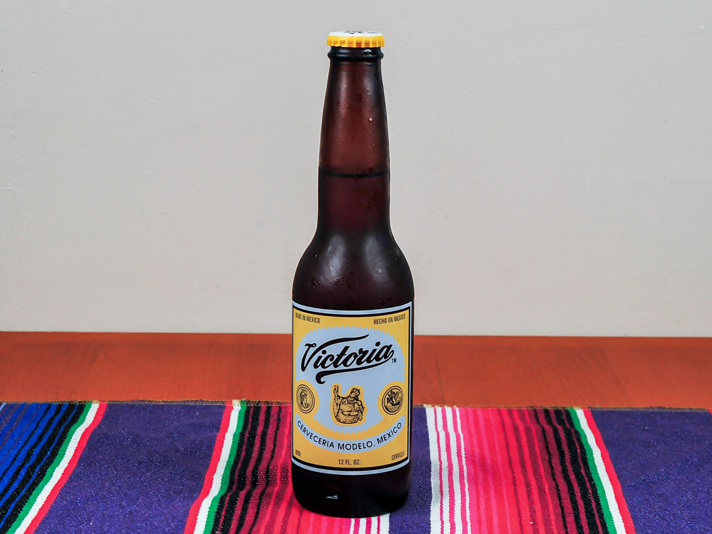 A bottle of Victoria beer with a yellow label, displayed on a colorful woven tablecloth.