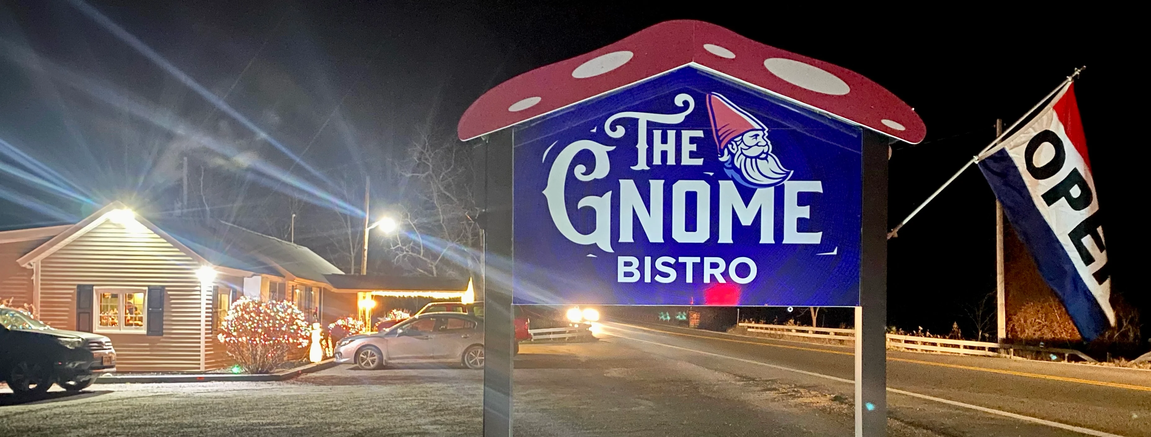 A brightly lit restaurant sign featuring a whimsical gnome design, welcoming visitors. The bistro is located in a cozy, inviting setting along a nighttime street.
