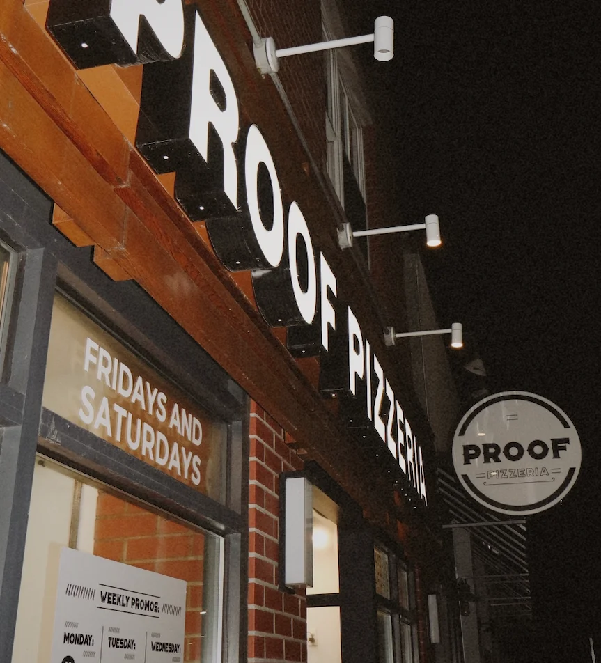 Exterior view of Proof Pizzeria with illuminated signage at night