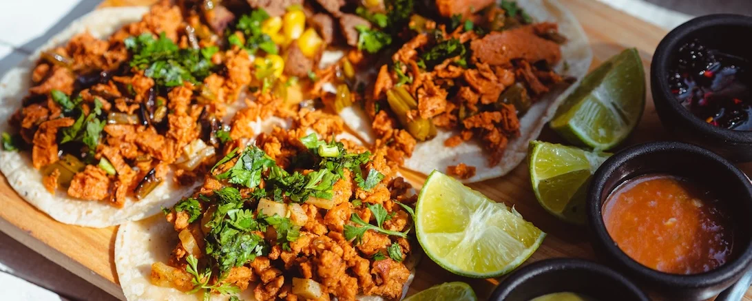 Al pastor tacos with cilantro and lime on a wooden board