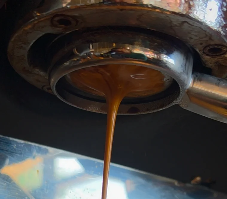 A delicious creamy shot of espresso brewing fresh from the machine though a bottomless filter, allowing the goldencontrast in color between crema and espresso.