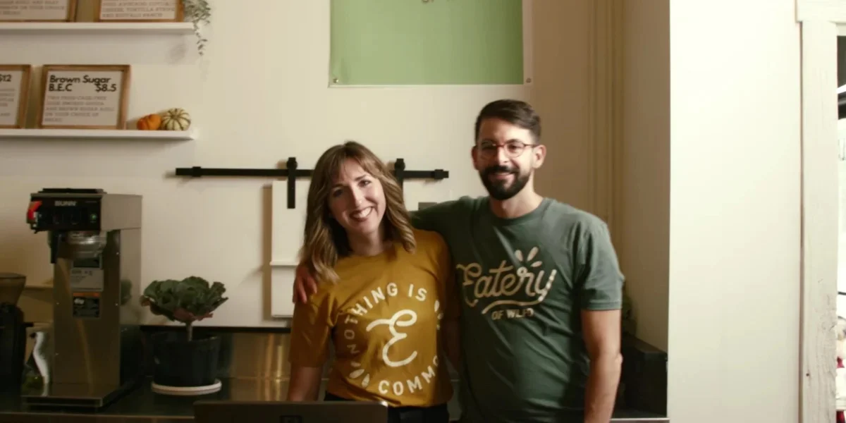 Two smiling restaurant owners posing in their cafe with coffee equipment.