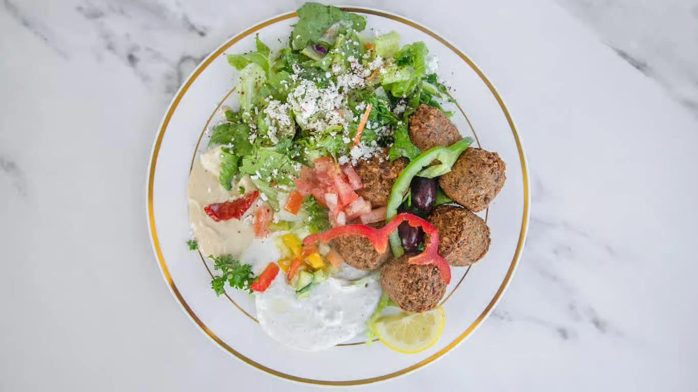 A colorful plate featuring falafel balls, fresh salad with tomatoes, greens, and a variety of vegetables, accompanied by lemon and a dip.