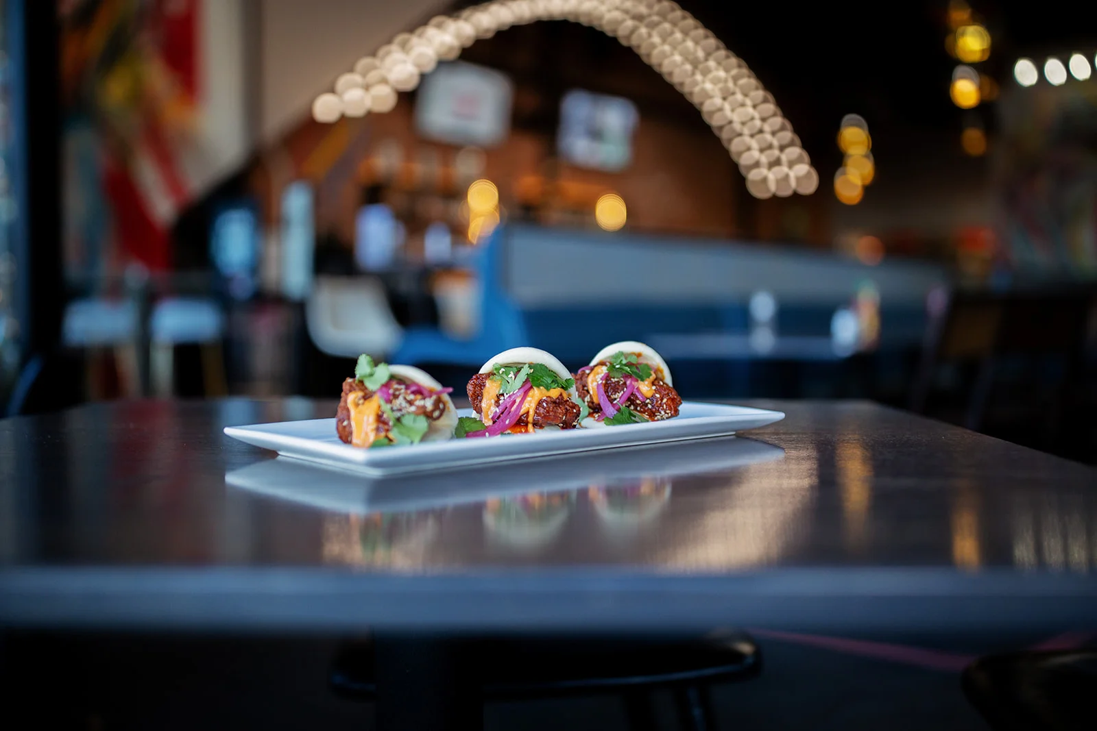 Three bao buns filled with fried chicken and garnished on a plate.
