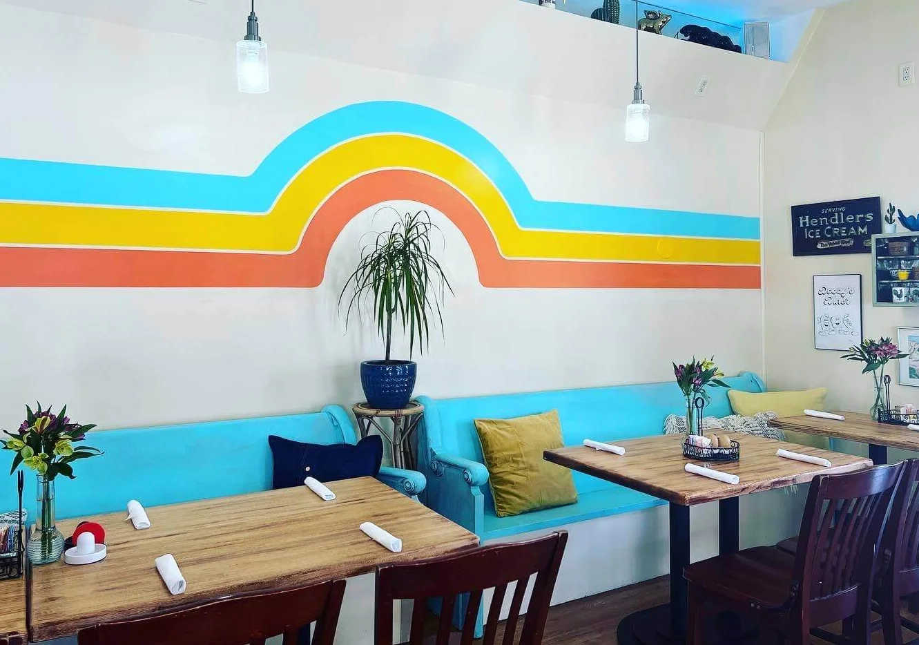 Image of the main dining room at Doozy's Diner, featuring a retro stripe pattern on the wall, tables set with roll ups, bright and cheery decor.