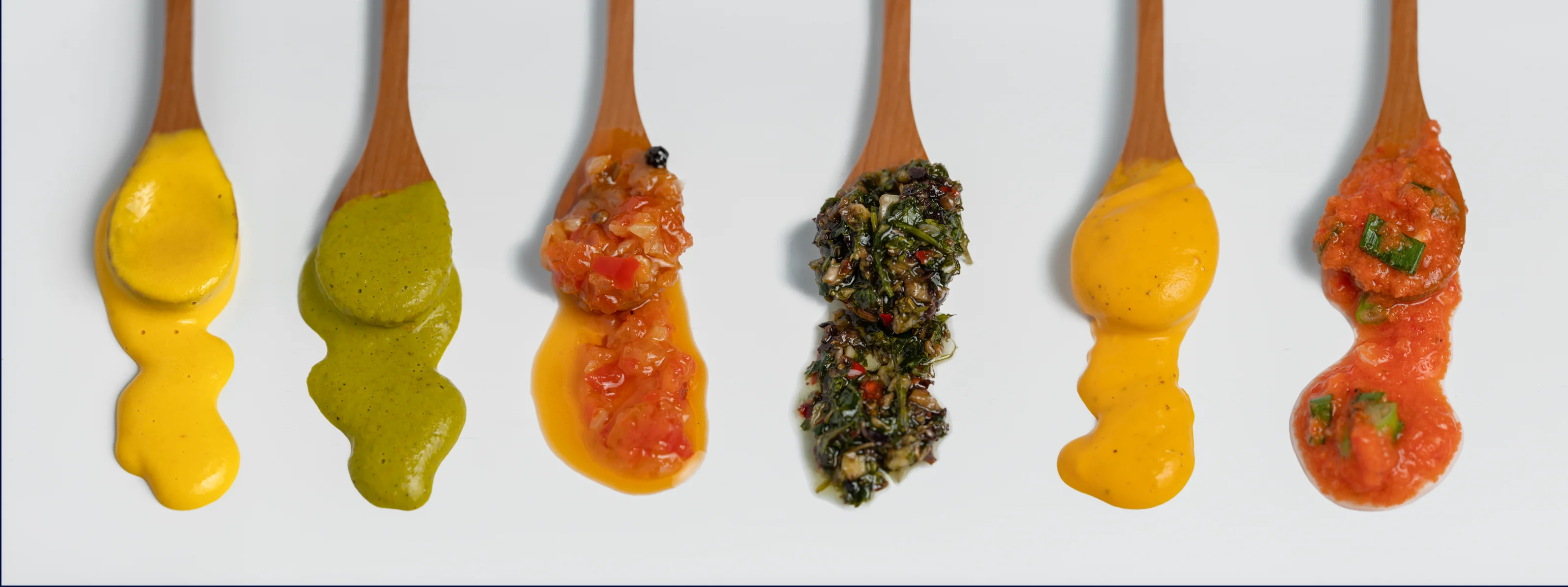 Assorted sauces in wooden spoons from various cuisines