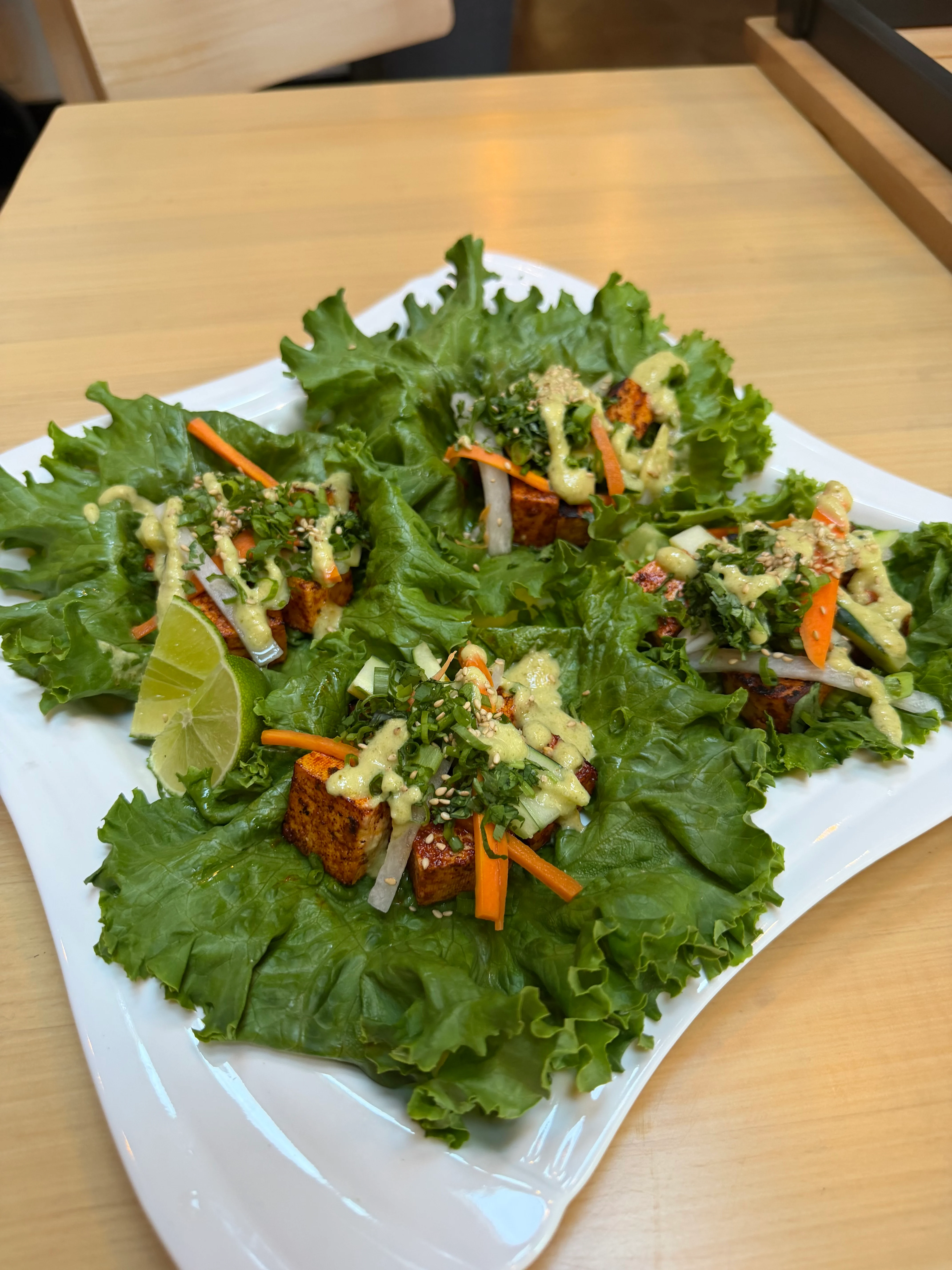 A vibrant plate of lettuce wraps filled with tofu, vegetables, and a drizzle of sauce, decorated with lime wedges.