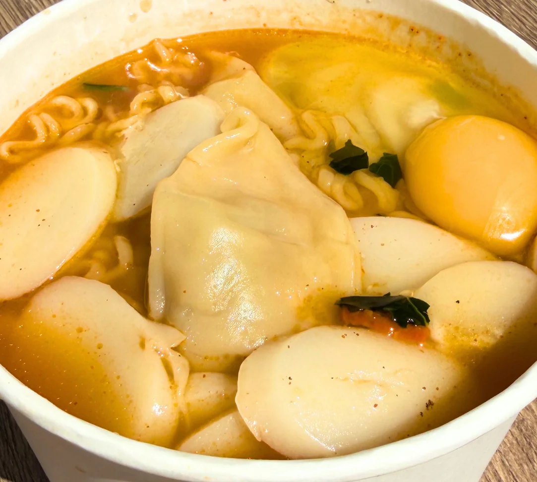 Bowl of spicy noodle soup with dumplings, egg, and rice cakes.