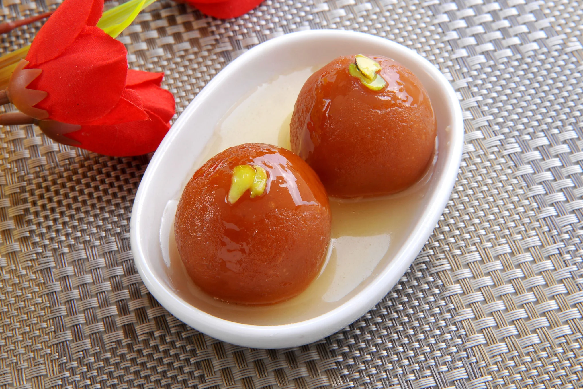A close-up of a vibrant gulab jamun dessert on a decorative plate.
