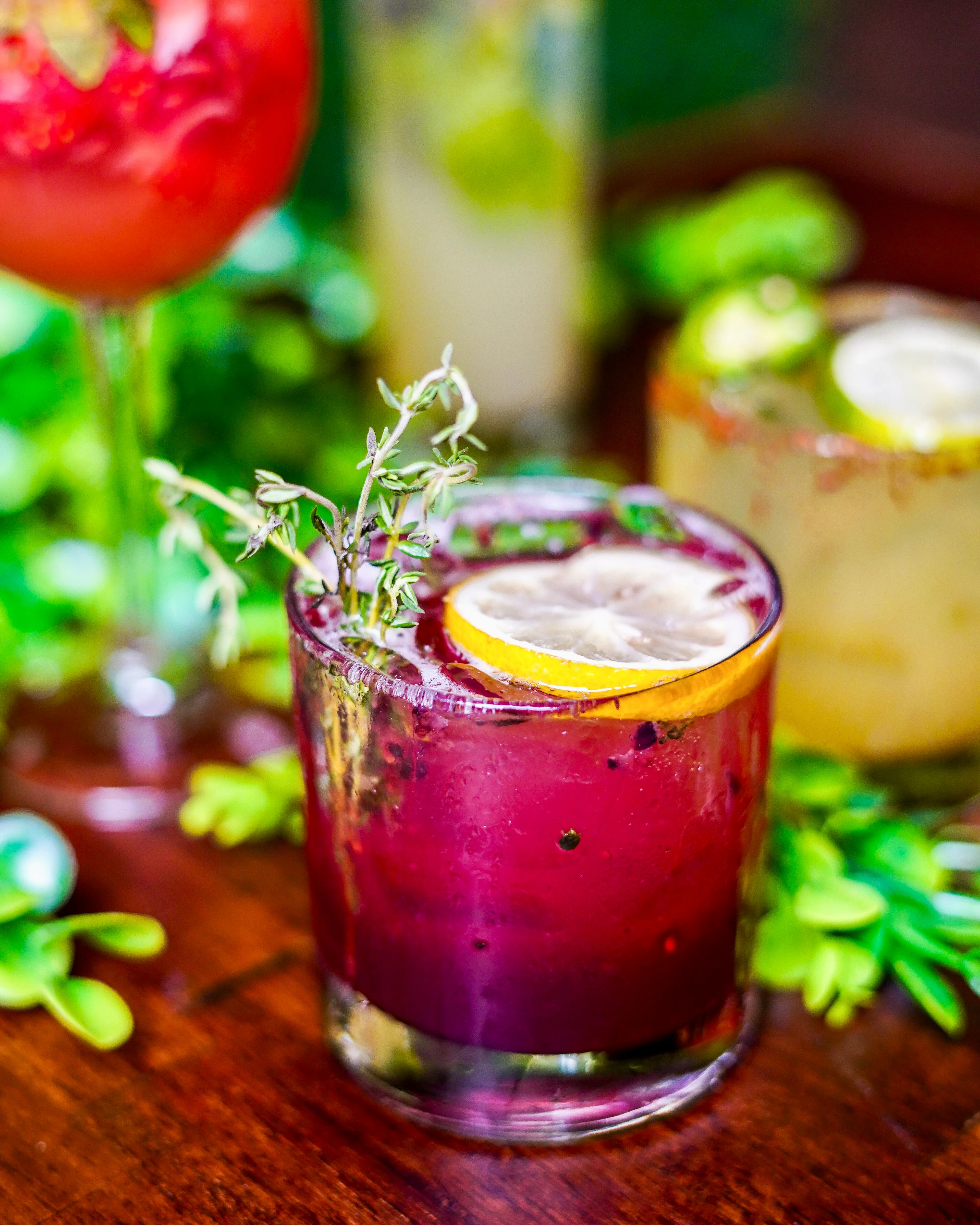Colorful cocktail with lemon and thyme garnish on a wooden table